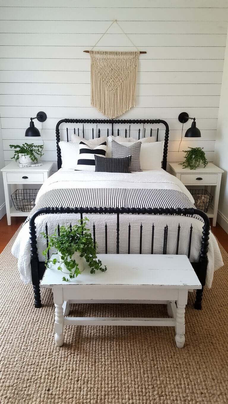 Cozy rustic modern bedroom with black spindle bed, white linens, striped quilt, macramé wall hanging, mismatched nightstands, trailing plants, and black and white accent pillows on a distressed white bench.